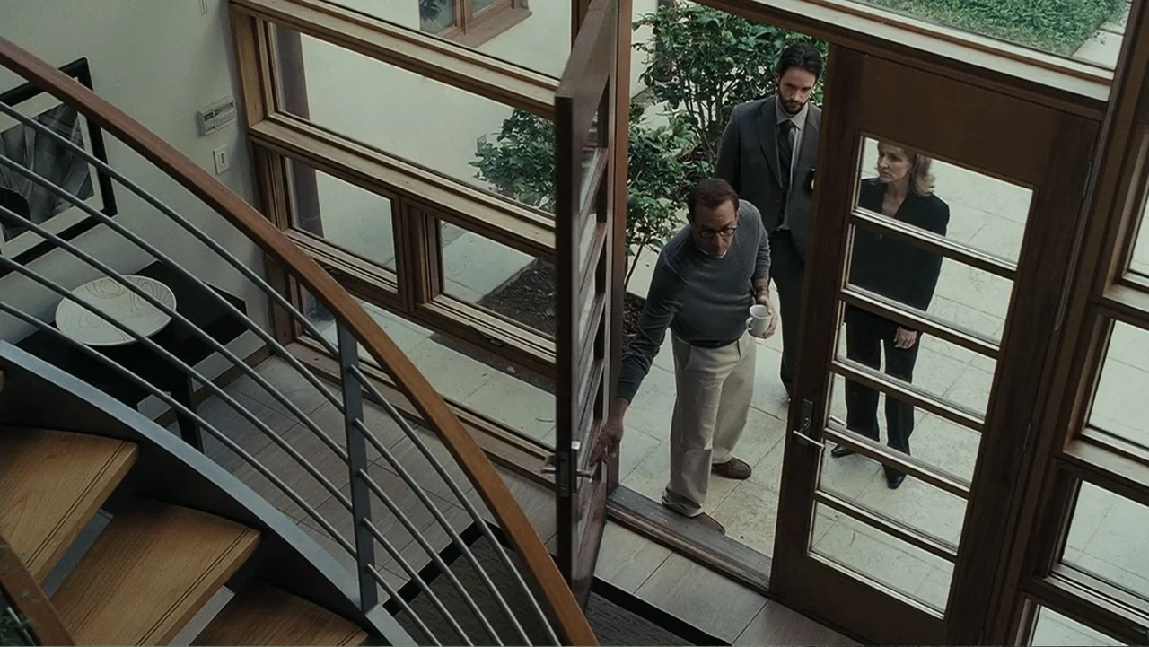 Mr. Brooks (2007) movie still: medium — A modern foyer with a spiral staircase has a large wooden glass-paned door. Three individuals stand in the…