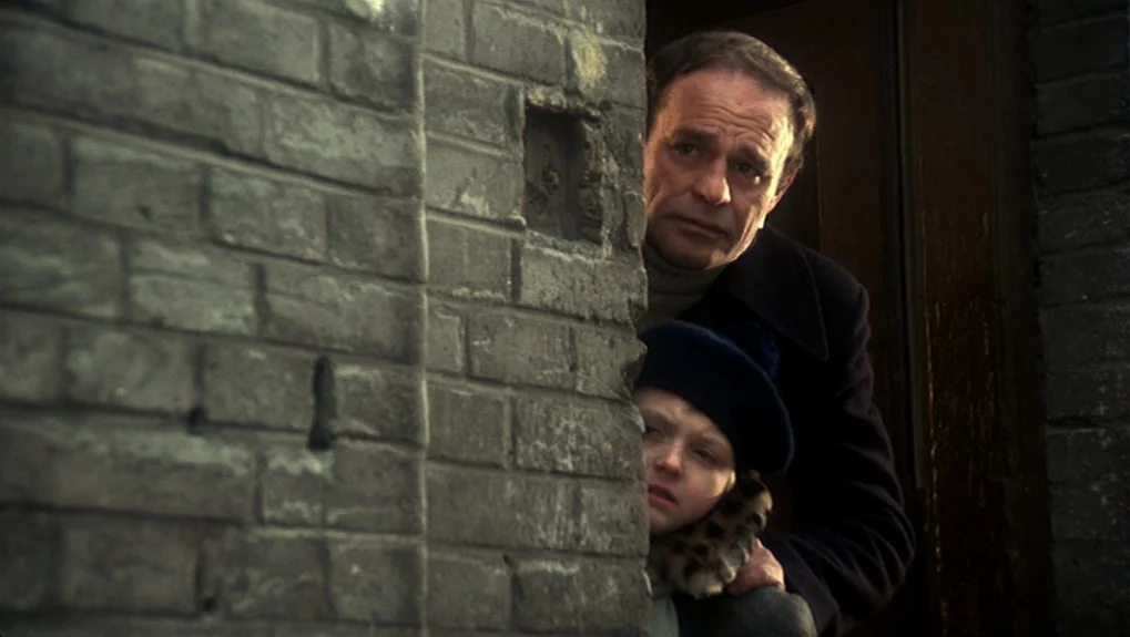 The War of the Worlds: Next Century (1981) movie still: medium — A man and a child stand behind the corner of a weathered brick building. The pair…