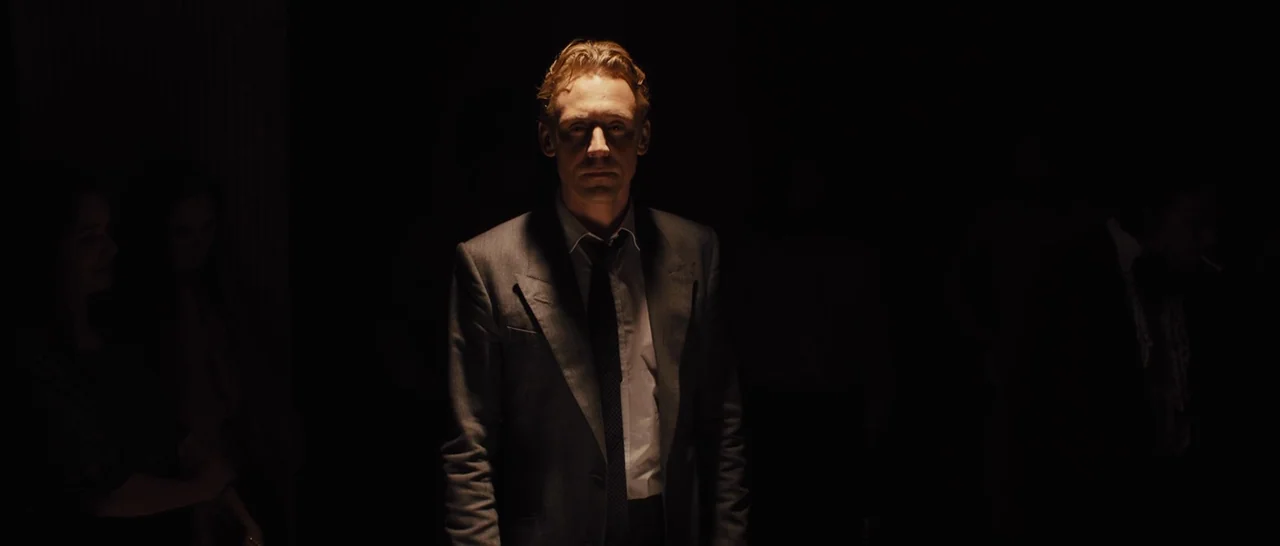 High-Rise (2015) movie still: medium — A man stands alone in a cavernous, pitch-black space with no other discernible features. He is illuminated by…