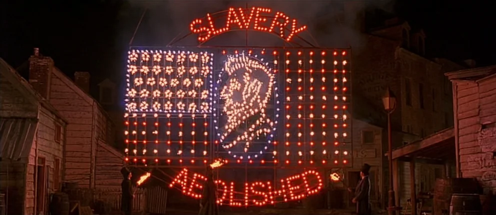 Gangs of New York (2002) movie still: wide — A 19th-century town square features a large illuminated sign with the text Slavery Abolished. Three…