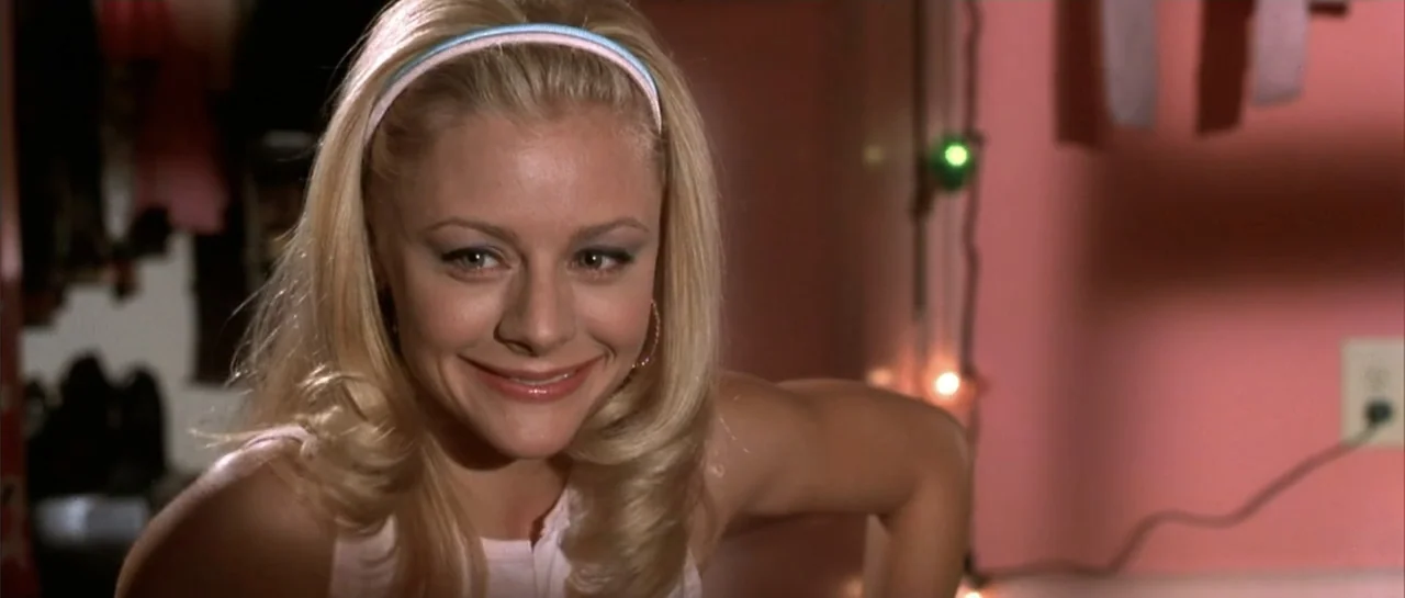Legally Blonde (2001) movie still: closeup — A bedroom features pink walls with decorative string lights visible in the blurred background. A young…