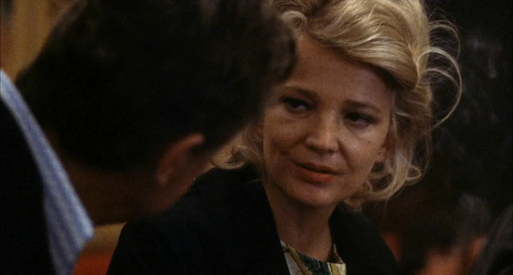 A Woman Under the Influence (1974) movie still: closeup — A dimly lit indoor space with blurred background elements suggest a social environment. A…