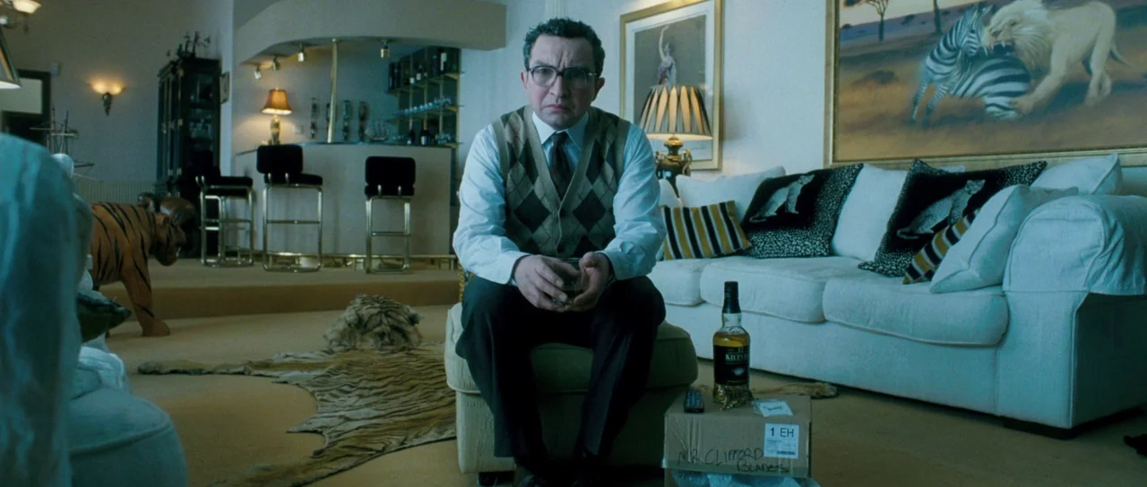 Filth (2013) movie still: medium — A spacious room features a white sofa, a wet bar, and tiger-themed decor. A man sits on an ottoman in the center…