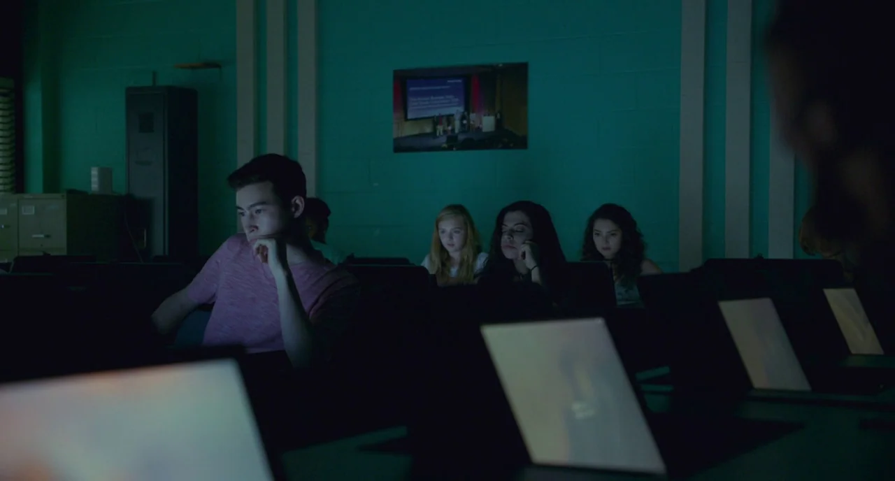 Eighth Grade (2018) movie still: medium — A dark computer lab features rows of laptops illuminating the faces of young students. The students look…