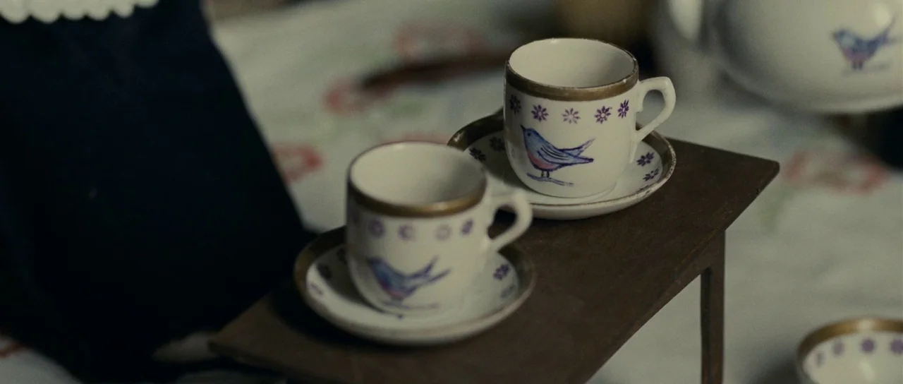 The Woman in Black (2012) movie still: closeup — A miniature wooden table holds two small ceramic teacups featuring bird patterns. A patterned…
