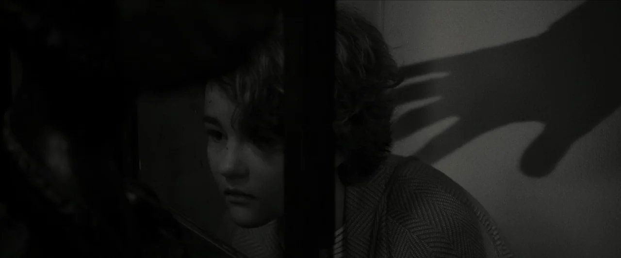 Wonderstruck (2017) movie still: closeup — A child peers through a narrow vertical gap in a dark structural frame. A large, dark shadow of a human…