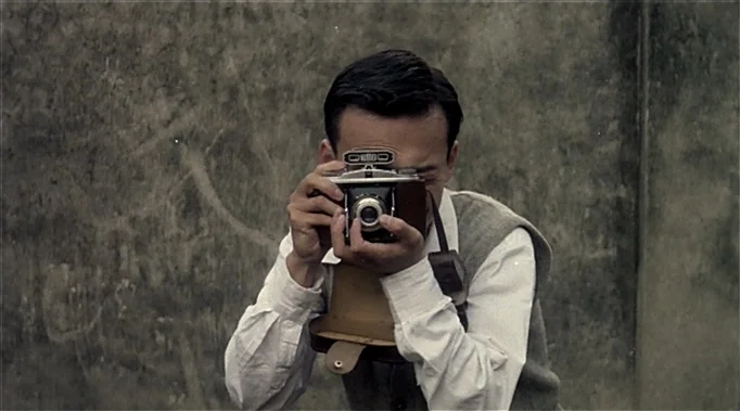 A Time To Love and A Time To Die (1985) movie still: medium — A man stands in front of a textured, mottled concrete or plaster wall. He holds a…