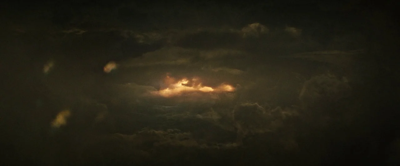 Alien: Romulus (2024) movie still: establishing — Dark storm clouds fill the frame with thick, layered formations. A bright amber light illuminates…