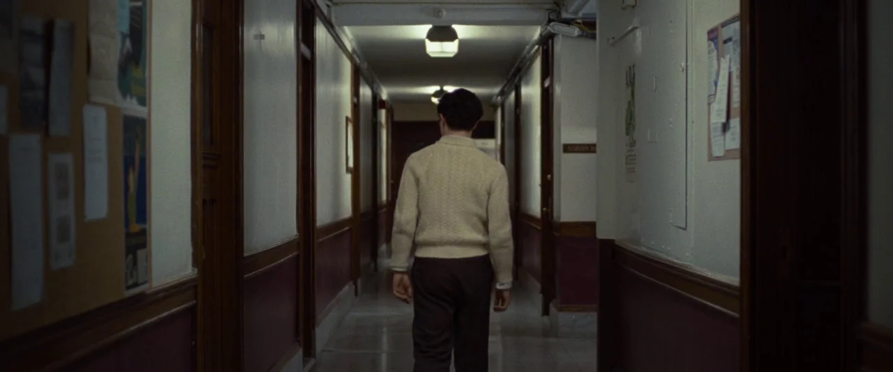Kill Your Darlings (2013) movie still: fullbody — A long, narrow hallway features wood-paneled wainscoting and bulletin boards mounted on white…