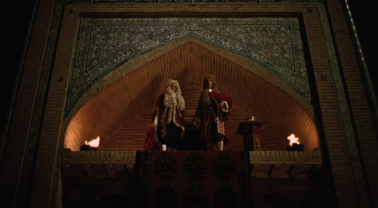 Orlando (1992) movie still: wide — An arched alcove with blue mosaic tiles sits elevated above a dark courtyard area. Two figures in historical…