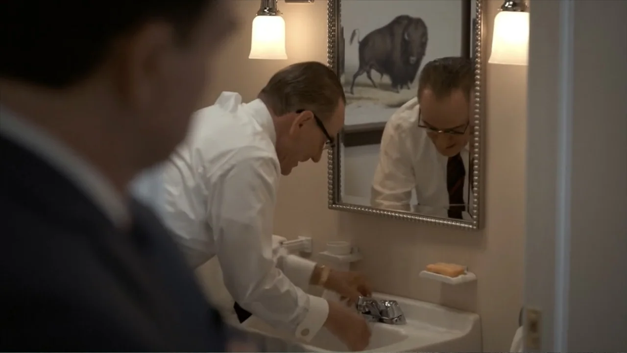 All the Way (2016) movie still: medium — A clean, modern domestic space with beige walls and a silver-framed mirror. A man in a white dress shirt…