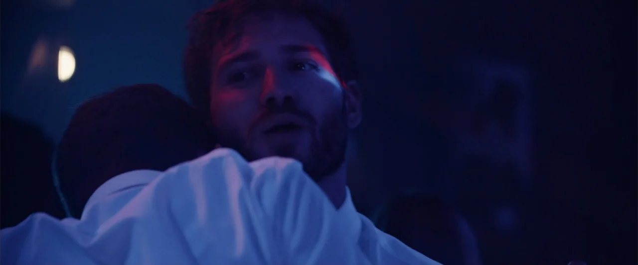 The Thorn On His Side (2014) movie still: closeup — A darkened interior space features blue and red light hitting the subjects. A bearded man in a…
