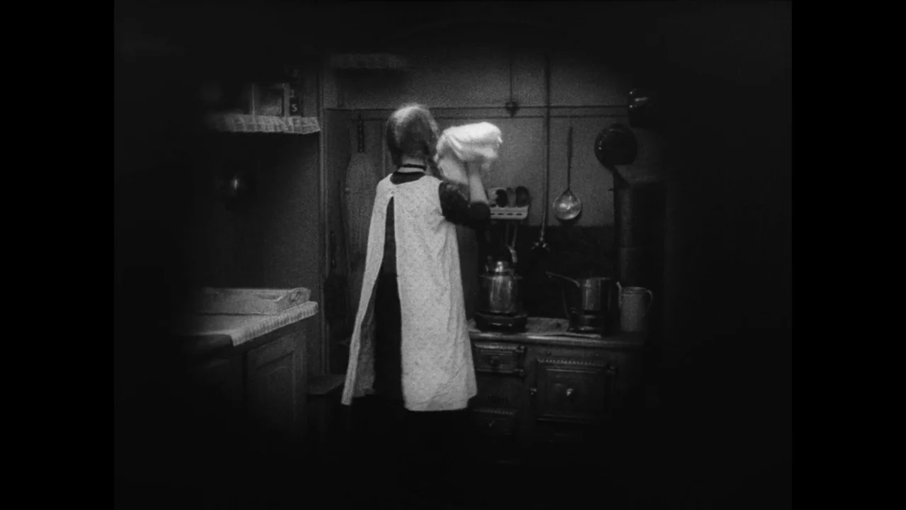 Master of the House (1925) movie still: medium — A dimly lit room contains a wood-burning stove and assorted hanging cooking utensils. A woman in an…