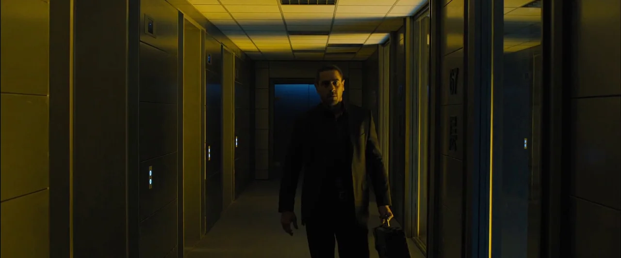Skyfall (2012) movie still: fullbody — A narrow office corridor features modern metal panels and illuminated vertical door strips. A man in a black…