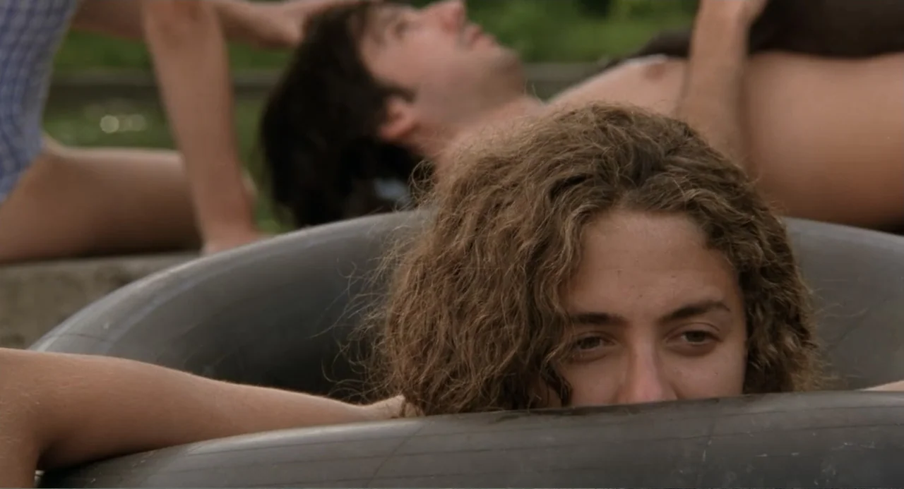 La Ciénaga (2001) movie still: closeup — A group of young adults relax in a swimming pool on a clear day. A person with curly brown hair rests their…