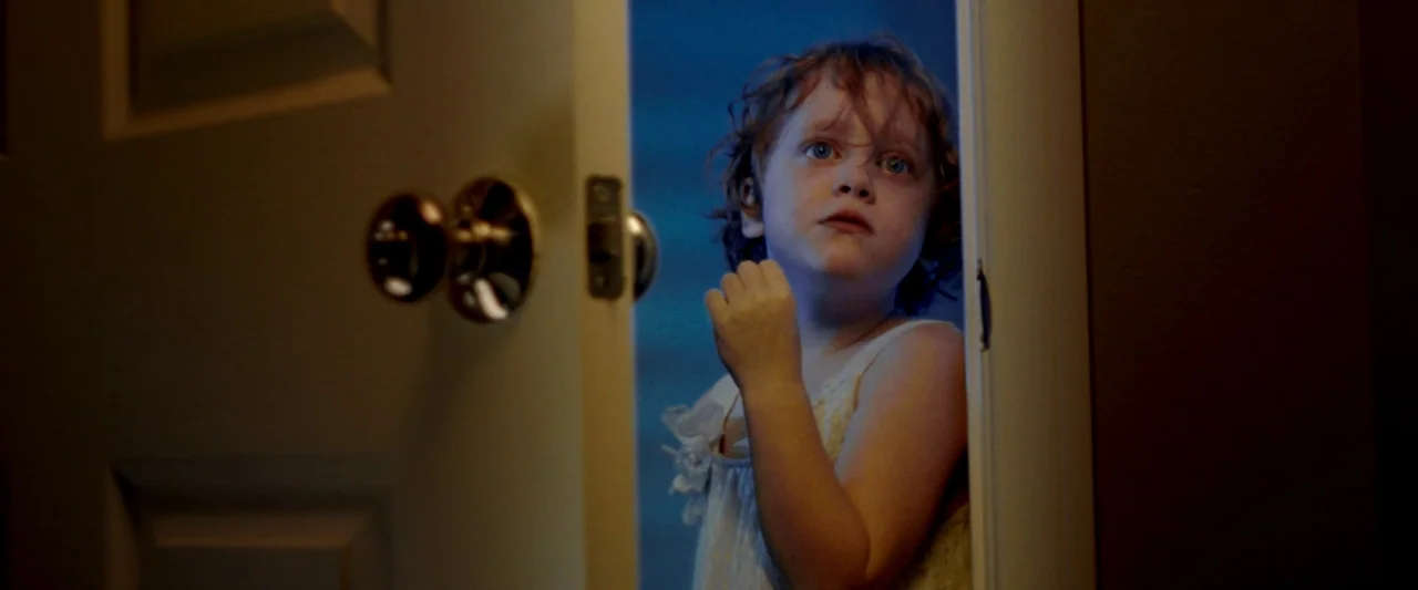Moon Garden (2022) movie still: medium — A young child stands in an open doorway of a dim residential space at night. The child looks past the…