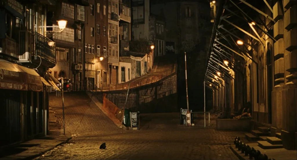 This Night (2008) movie still: establishing — A quiet, narrow European street at night features aged stone buildings and cobblestone pavement. Rows…