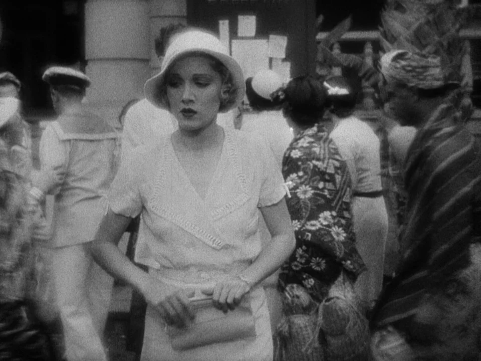 Island of Lost Souls (1932) movie still: medium — A bustling public space features a woman surrounded by pedestrians and a notice board. The woman…