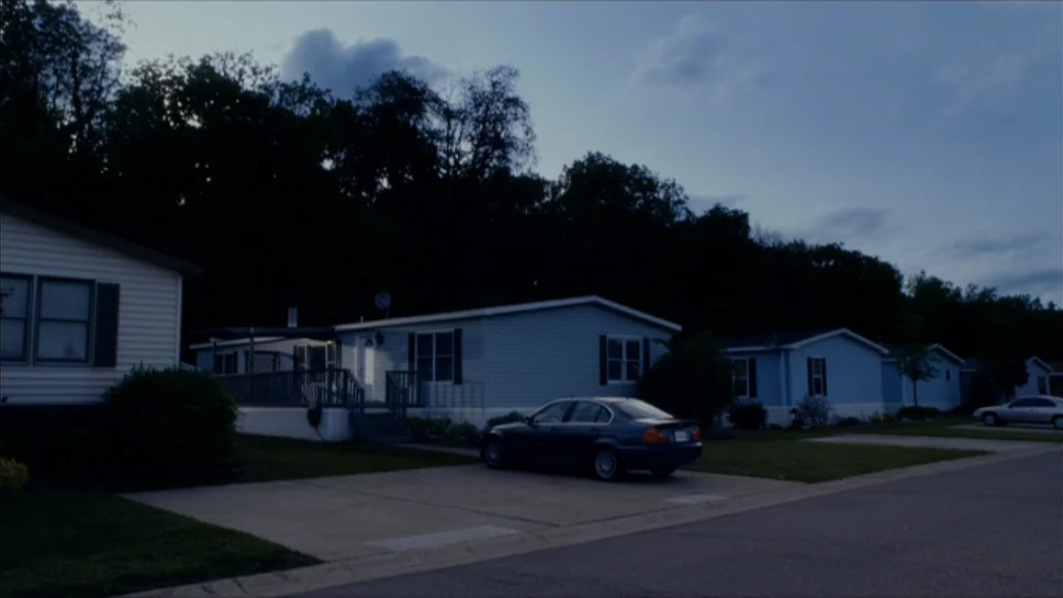 Youth In Revolt (2009) movie still: establishing — A suburban mobile home park under a deep blue twilight sky with dense trees. Several single-story…