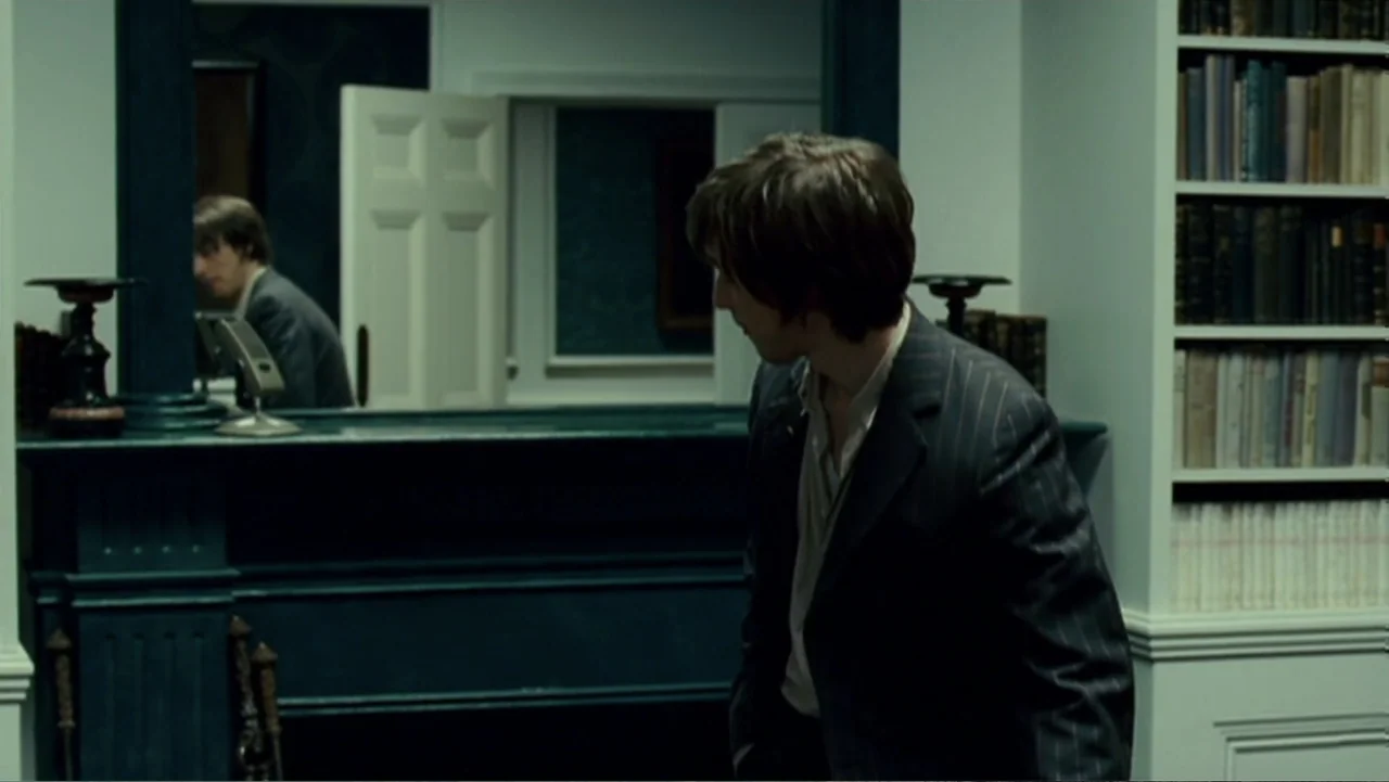 Penelope (2007) movie still: medium — A dark-toned study features a fireplace, a bookshelf, and a large wall mirror. The man in a pinstripe suit…