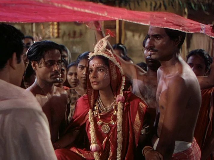 The River (1951) movie still: medium — A group of people gathers in a rustic outdoor setting under a red cloth. A woman dressed in traditional…