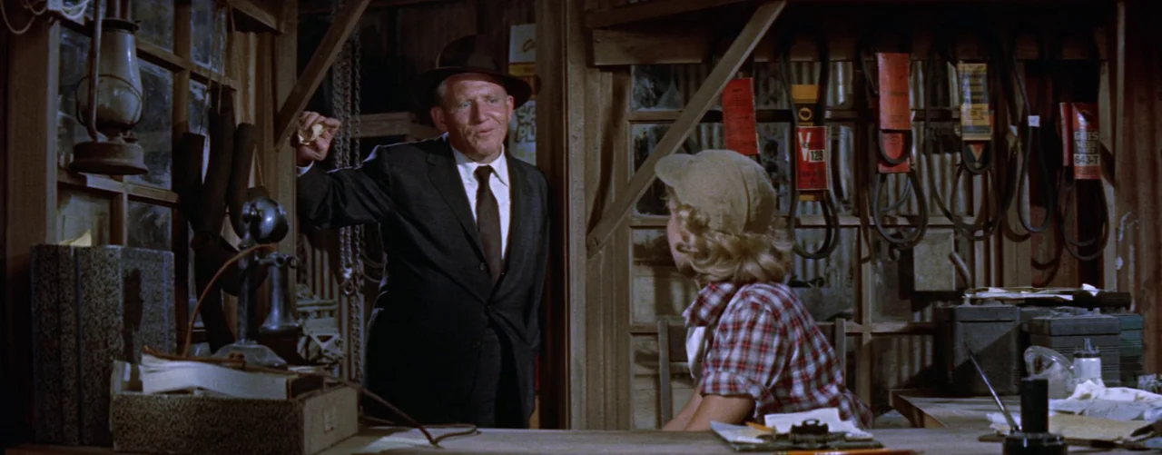 Bad Day At Black Rock (1955) movie still: medium — A rustic workshop features wood-paneled walls lined with hung belts and automotive equipment. A…