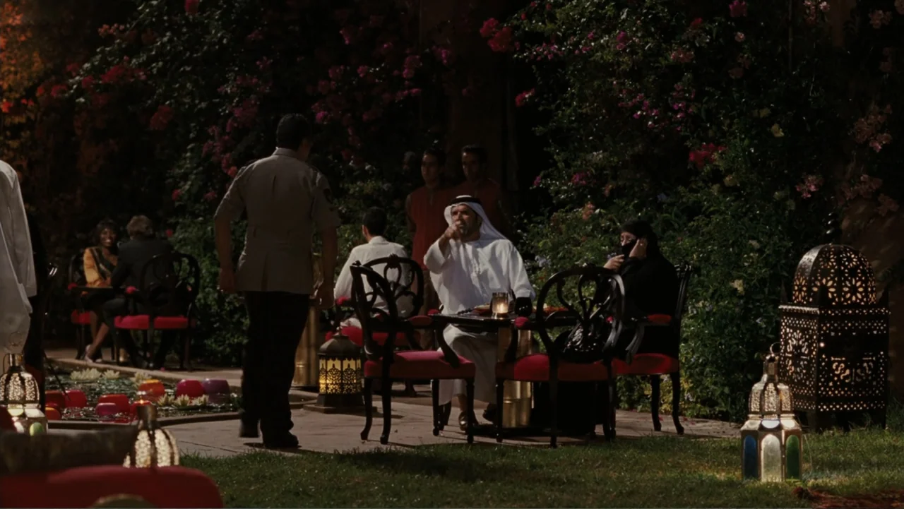 Sex and the City 2 (2010) movie still: medium — An outdoor evening setting features tables with ornate metal lanterns nestled against a flower wall.…