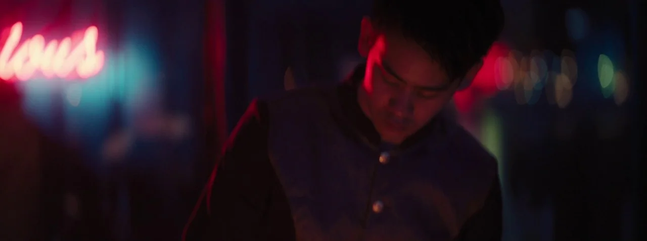 Dead Pigs (2018) movie still: medium — A dimly lit room with glowing neon signage reflecting off dark surfaces. A young man wearing a dark jacket…