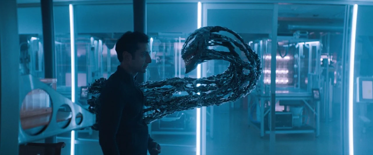 Venom (2018) movie still: medium — A high-tech laboratory features glass partitions and large metal containment units in the background. A man…