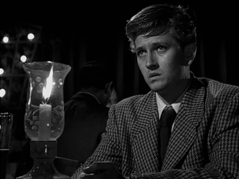 The Big Night (1951) movie still: medium — A dimly lit table area within a restaurant setting at night. A young man sits in the foreground beside a…