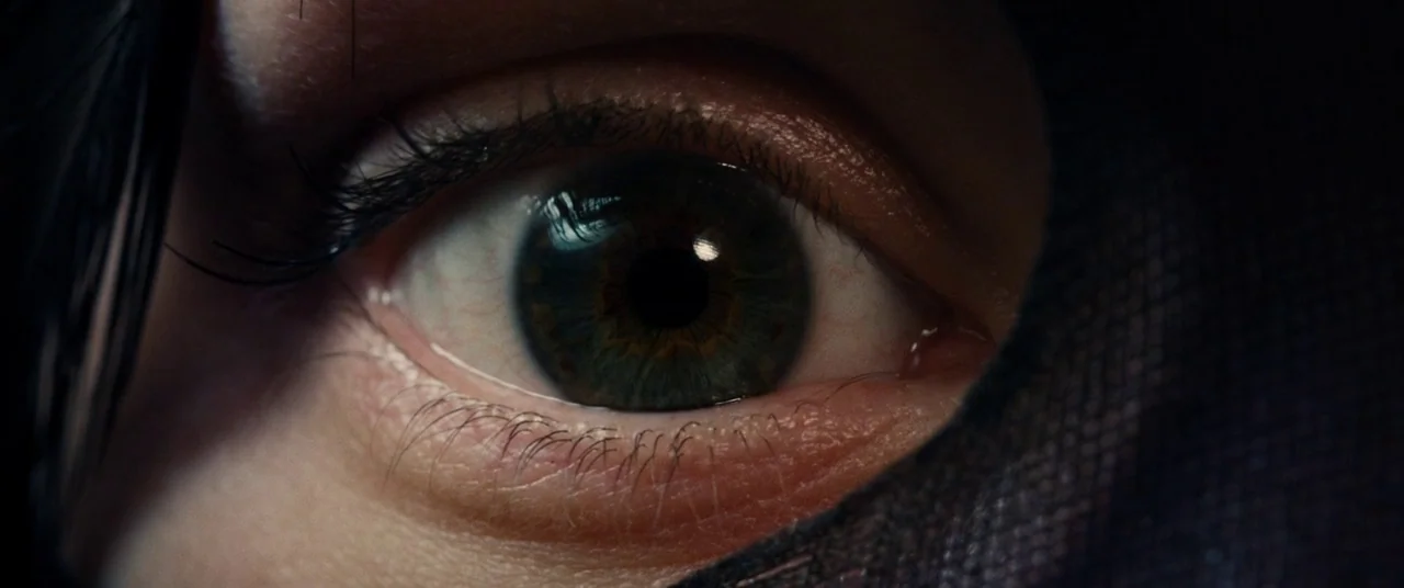 I Origins (2014) movie still: closeup — A close-up view of a single human eye framed by dark, textured fabric. The iris is detailed with blue-green…