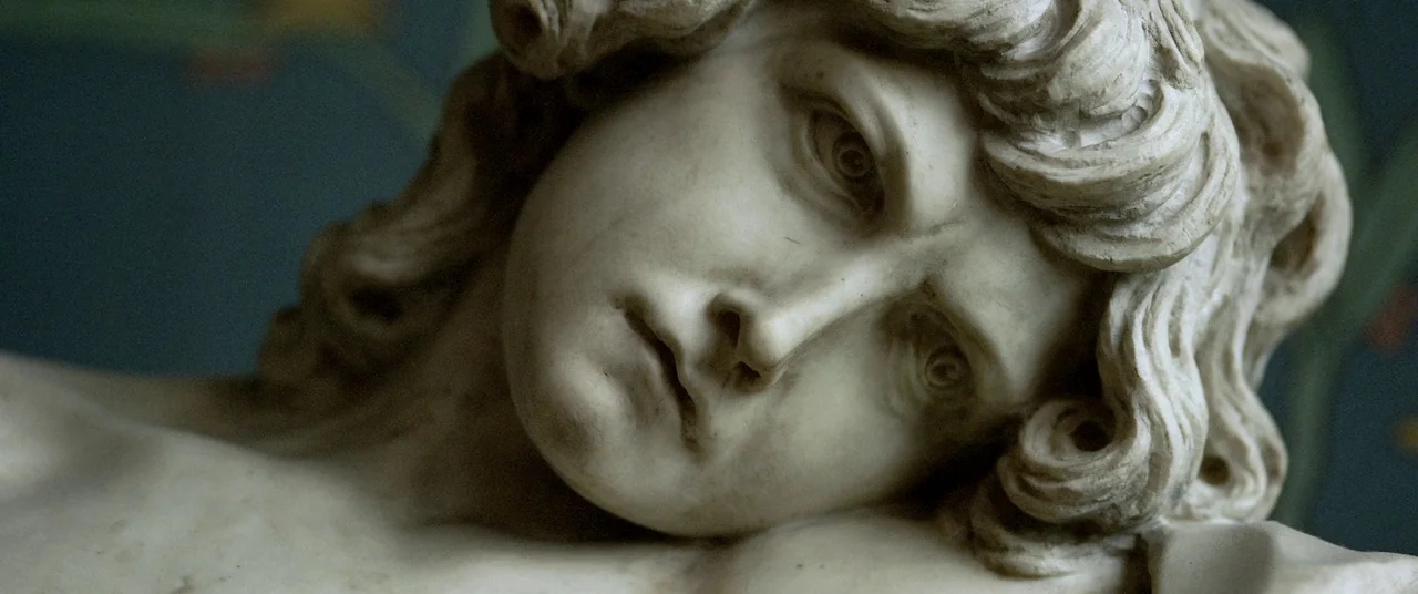 Samsara (2011) movie still: closeup — A marble statue head lies against a dark blue background with faint floral patterns. The sculpture features…