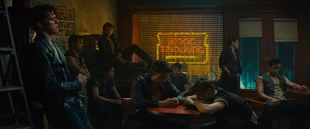 Making of: West Side Story (2021) movie still: wide — A dim 1950s style diner at night with a bright neon sign in the window. A group of men in…
