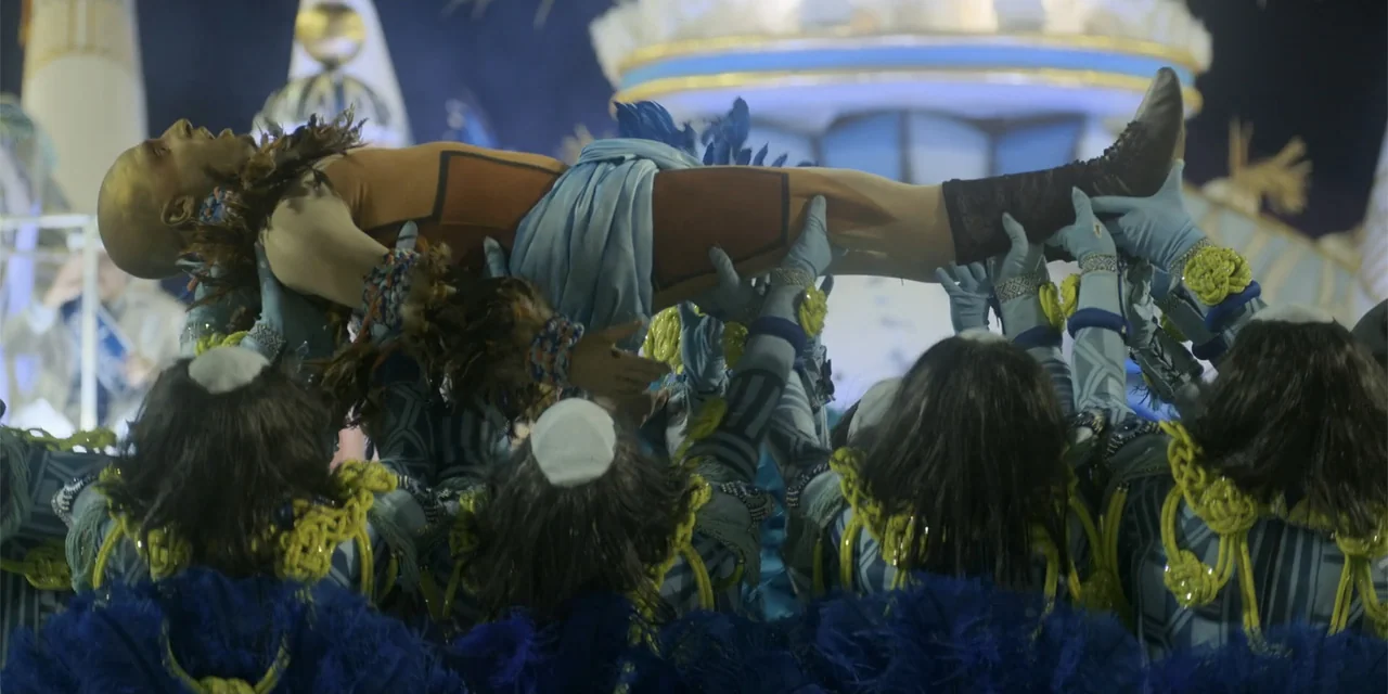 An Unforgettable Year - Summer (2023) movie still: medium — A group of dancers in blue and yellow costumes lift a performer at night. The performer…