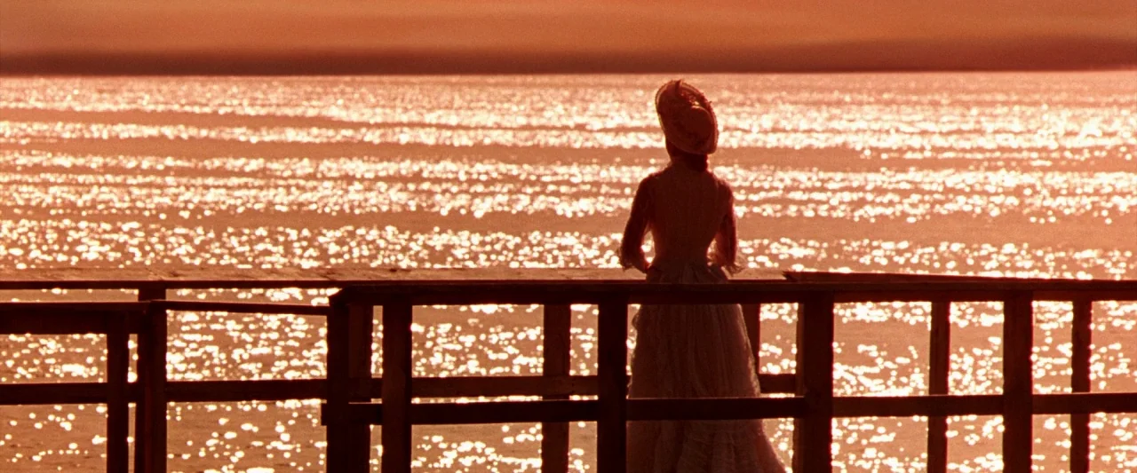The Age of Innocence (1993) movie still: fullbody — A wooden dock stretches across the foreground against a vast expanse of water. A woman in period…