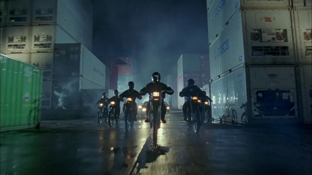 Hard Boiled (1992) movie still: wide — A night scene in a shipping container yard filled with stacks of metal crates. A group of motorcyclists…