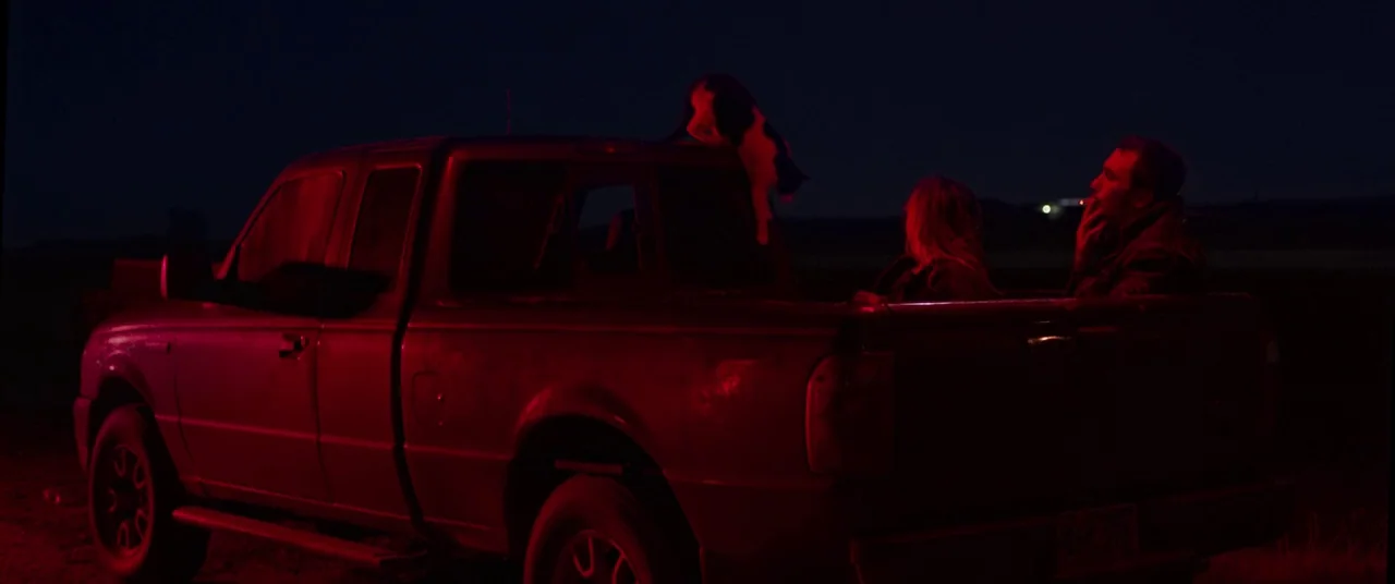 The Rider (2017) movie still: wide — A pickup truck is parked in a dark field under the night sky. A man and woman sit together in the back of the…
