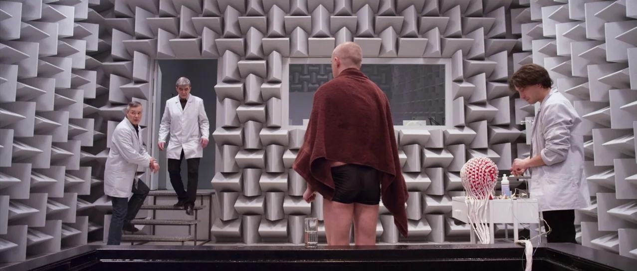 Vanishing Waves (2012) movie still: medium — A laboratory anechoic chamber lined with uniform grey acoustic foam wedges on all walls. A bald man…