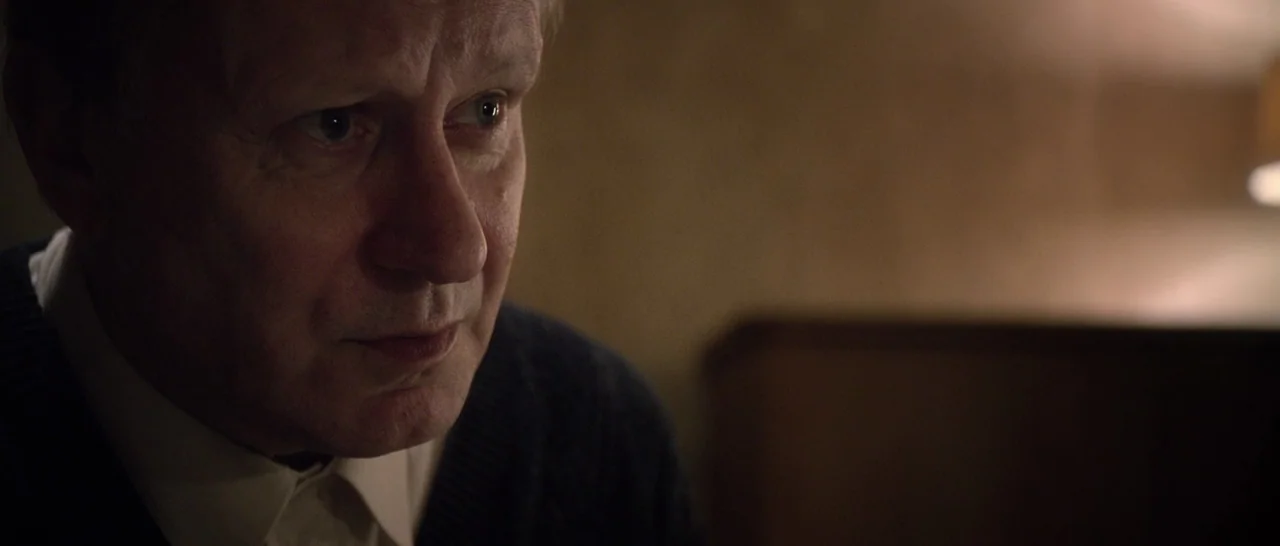 Nymphomaniac Vol 1 (2013) movie still: closeup — A dimly lit room with a textured wall and out-of-focus background furniture. An older man gazes…