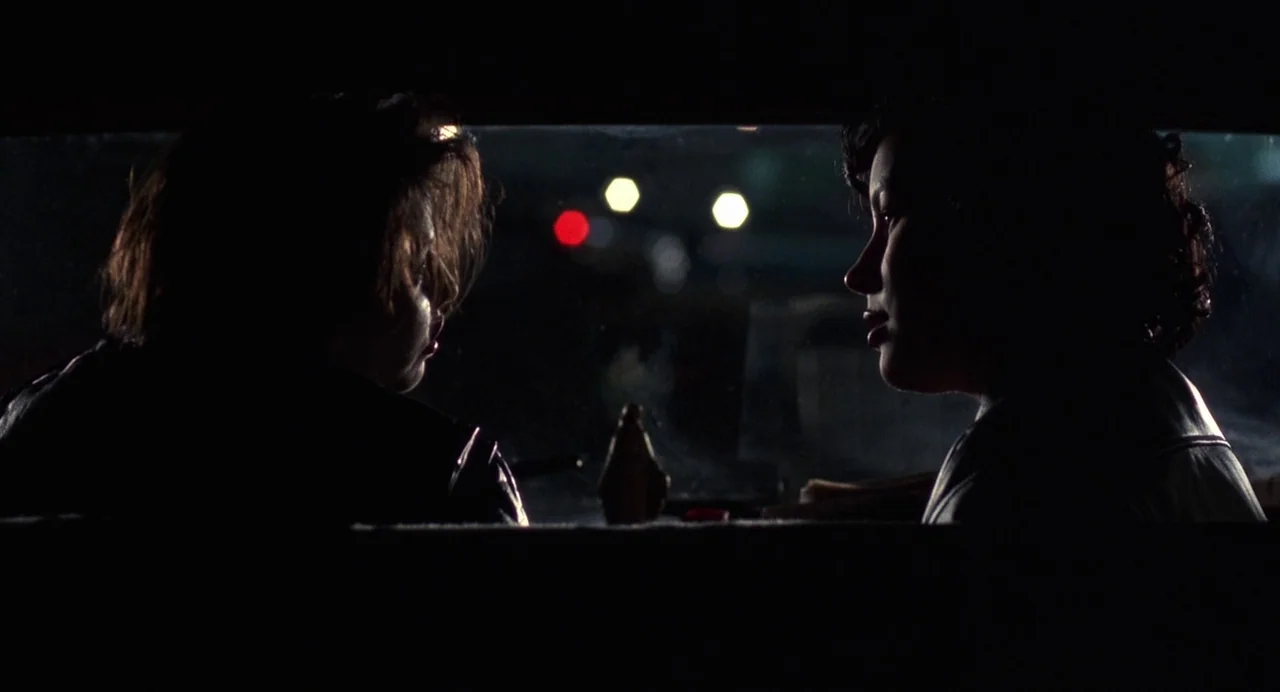 Bound (1996) movie still: medium — Two people are silhouetted inside a vehicle at night. Streetlights blur through the back window behind them.
