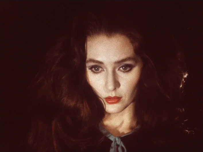 The Death of Maria Malibran (1972) movie still: closeup — A dark environment surrounds a woman with voluminous auburn hair and red lipstick. She…