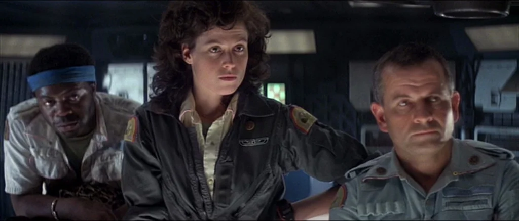 Alien (1979) movie still: medium — A dimly lit industrial cockpit with metallic paneling and electronic instrumentation in the background. Three…