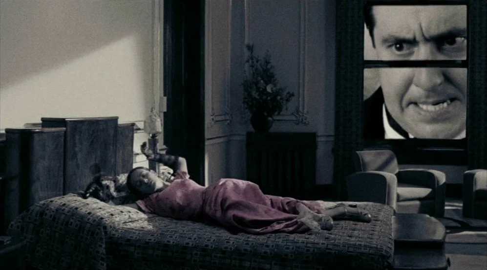 Frida (2002) movie still: wide — A dark hotel room features a woman lying on a bed. Outside the window, a colossal, disembodied face looms over the…
