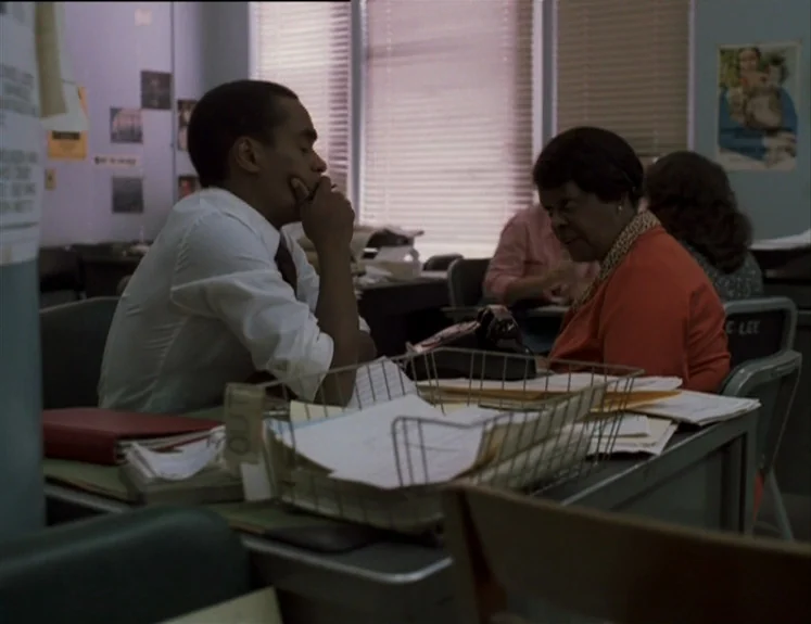 The Brother From Another Planet (1984) movie still: medium — An administrative work environment features gray metal desks and window blinds. A man…