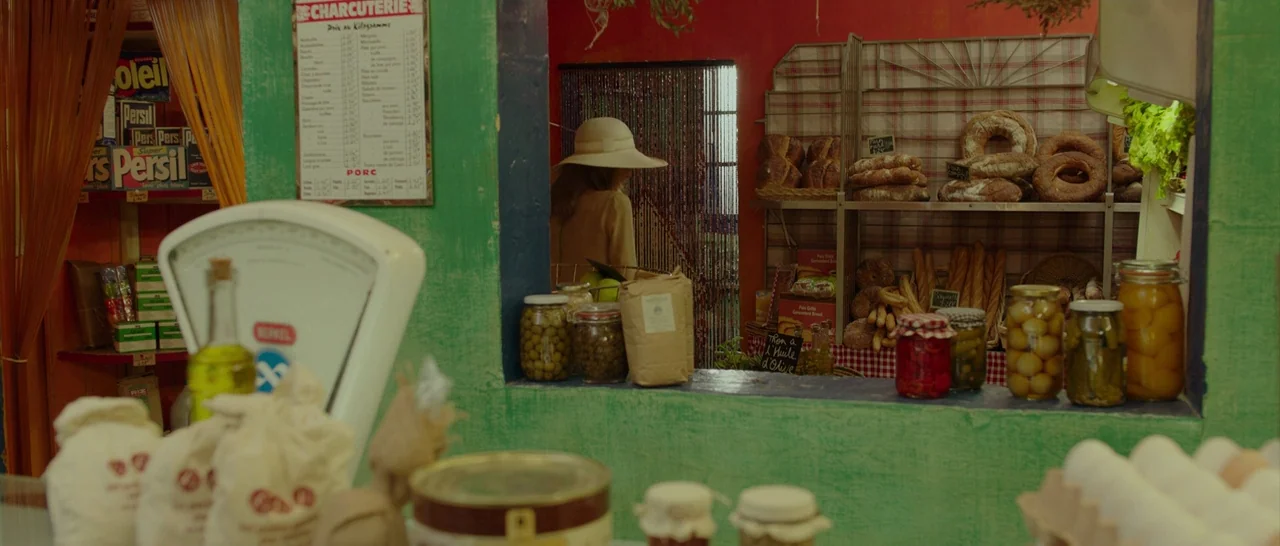 By The Sea (2015) movie still: medium — A small grocery store with vibrant green walls and shelves stocked with artisanal goods. A woman wearing a…