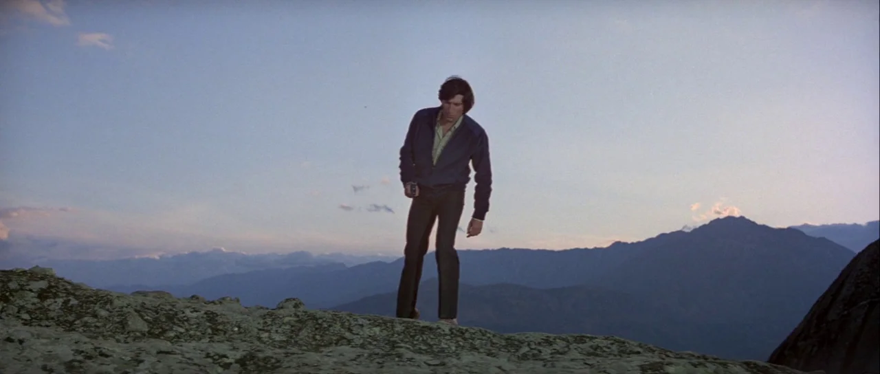 For Your Eyes Only (1981) movie still: fullbody — A high, barren mountain ridge stretches across the frame beneath a clear horizon. A man stands on…