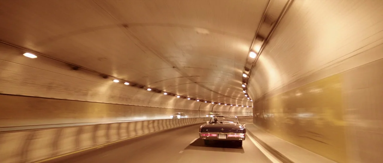 Knight of Cups (2015) movie still: wide — A long curved tunnel features yellow tiled walls and a repeating row of lights. A dark vintage convertible…