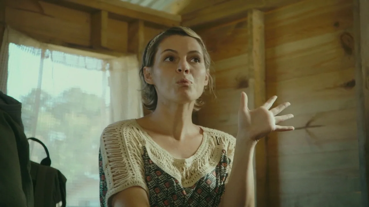 The Sacrament (2013) movie still: medium — The interior walls are constructed from exposed pine wood planks. A woman stands in the center gesturing…