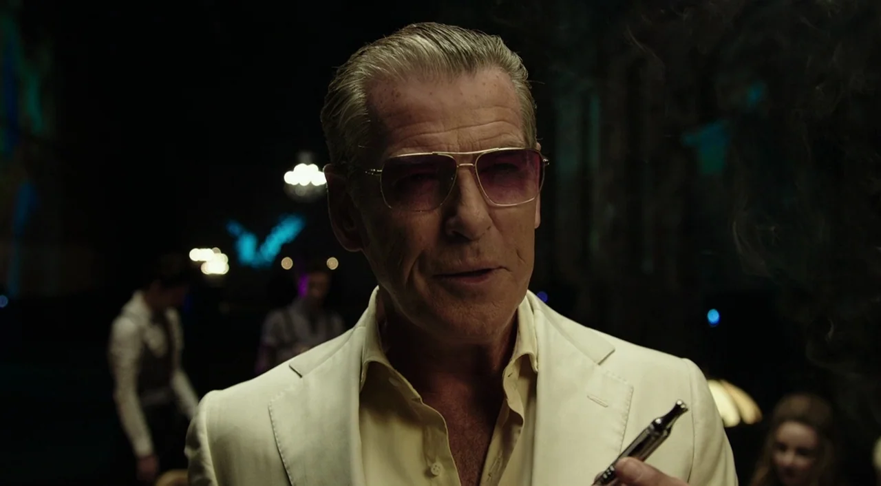 Urge (2016) movie still: medium — A dimly lit club interior features blurred out-of-focus background figures and muted colors. A man in a light suit…