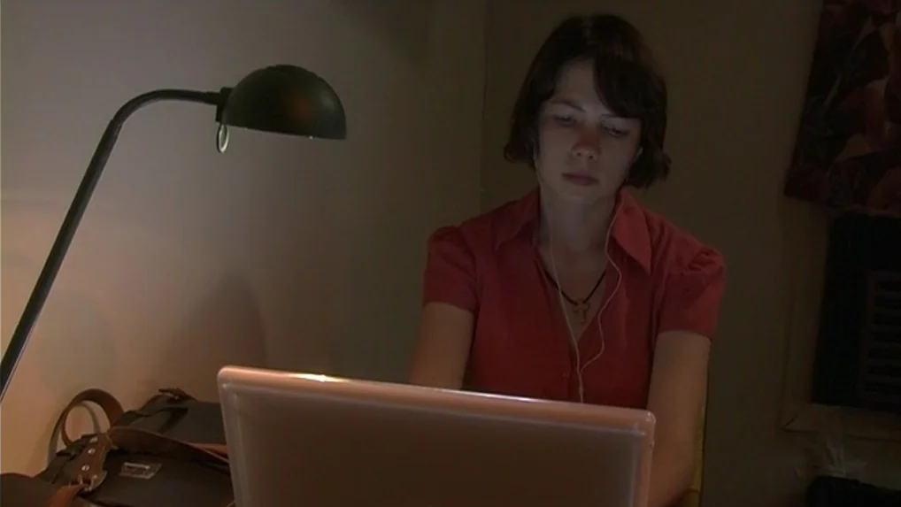 Land of Plenty (2004) movie still: medium — A dimly lit room contains a person working at a desk late at night. The subject faces a laptop screen…